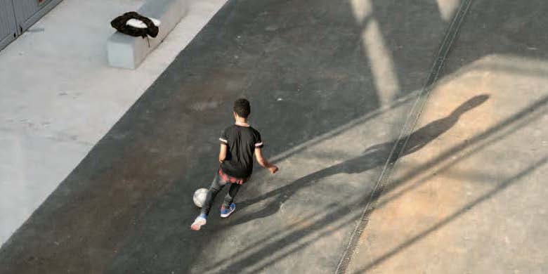 junger mann spielt fussball auf asphalt