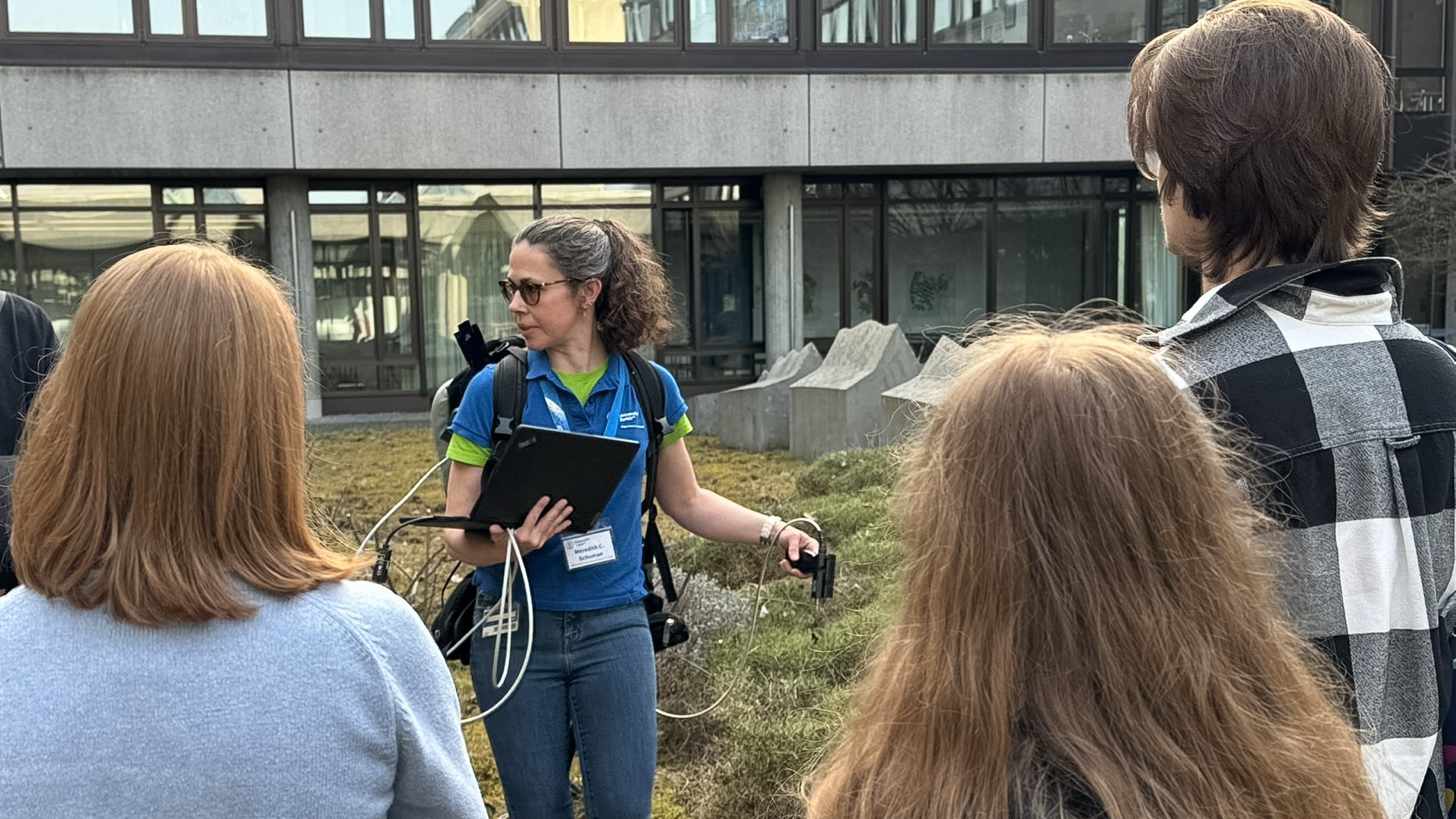 Eine Wissenschaftlerin demonstriert einen Feld Spectroradiometer . Der Spectroradiometer ist auf dem Rücken und hat viele Schläuche, die um den Körper herum verlaufen.