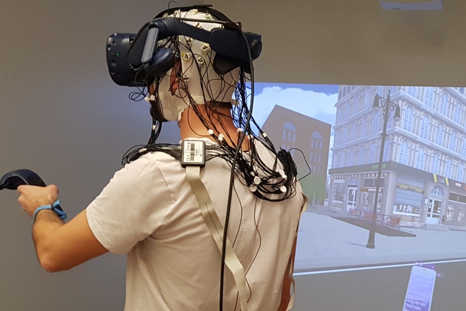 The world a test participant is experiencing wearing the HMD VR over an EEG cap is projected onto a large, screen-based CAVE VR system. Photo credit: GIVA